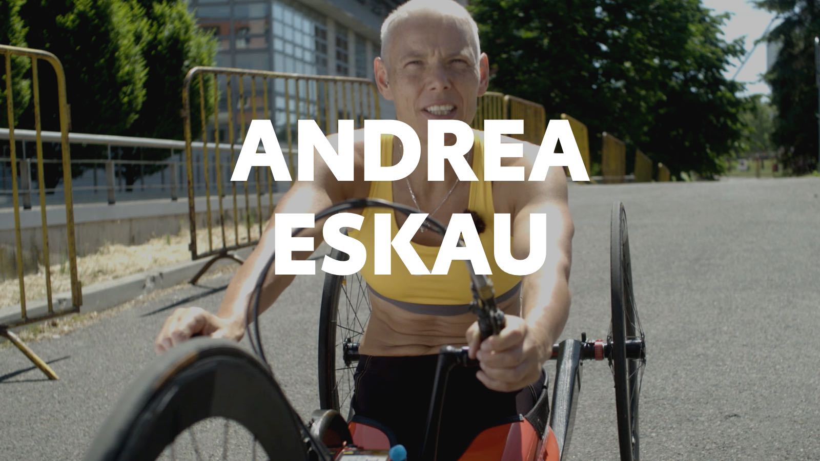 Andrea Eskauová v červenej pretekárskej kombinéze s bežkárskymi palicami v rukách sa pozerá priamo do objektívu.